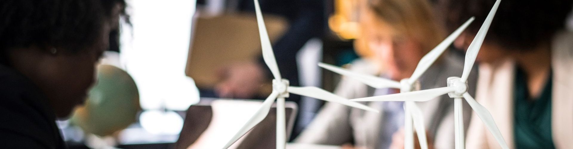 Team members gathered at a table discussing a scale model of turbines.